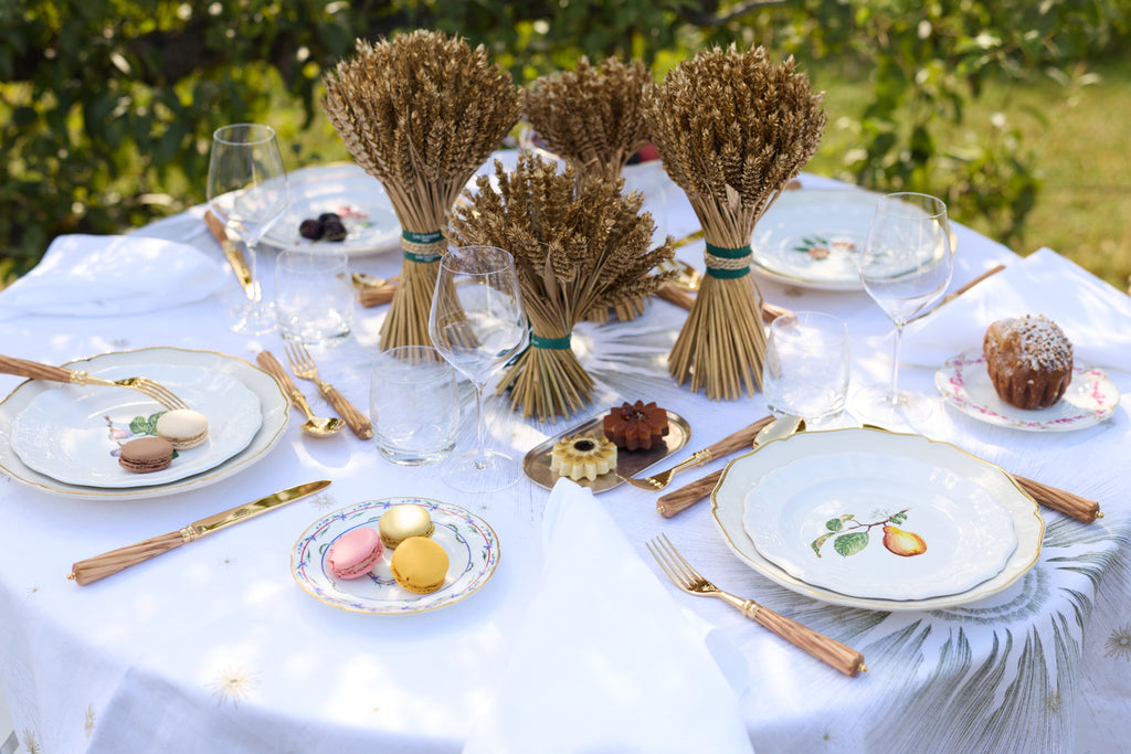 Z.d.G. Le Potager du Roi Stardust embroidered white linen tablecloth set on an outdoor table with desserts and wheat sheaves.