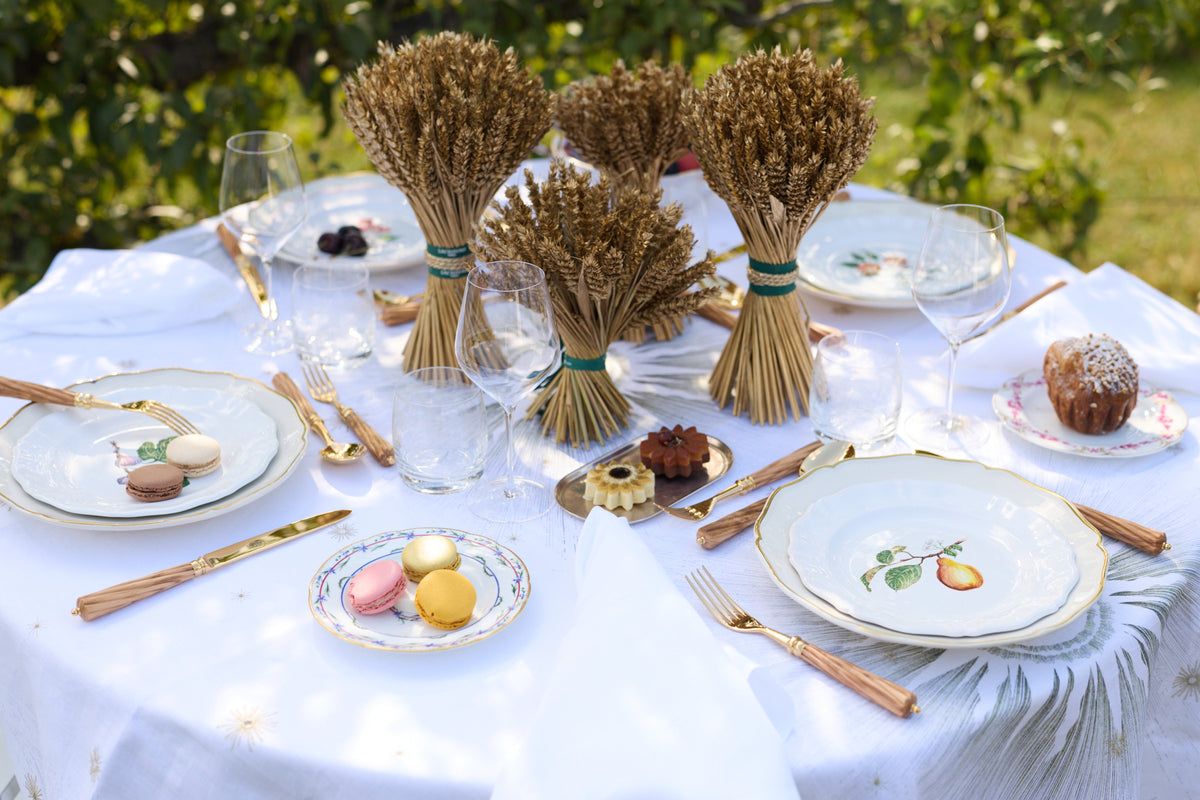 Z.d.G. Le Potager du Roi Stardust embroidered white linen tablecloth set on an outdoor table with desserts and wheat sheaves.