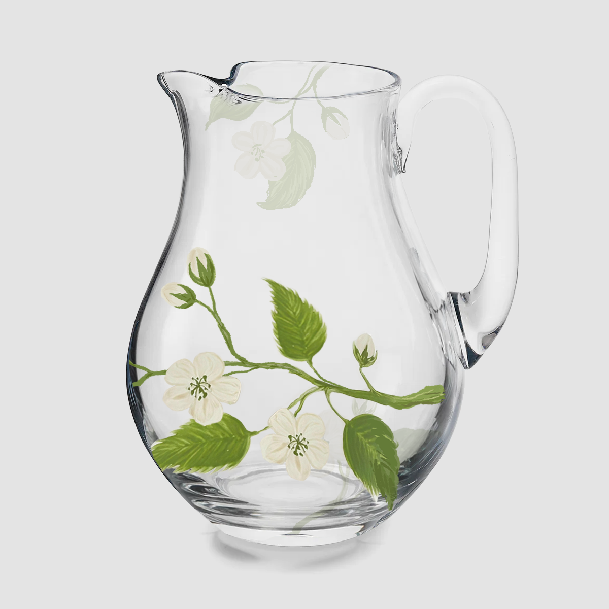 A product photograph of a clear glass pitcher with an elegant, curved silhouette and a wide pouring spout. The glass is delicately hand-painted with a botanical design featuring a slender branch with bright green leaves and a single, detailed green apple. The jug is shown empty against a clean, neutral background.