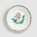 A top-down product photograph of a white round ceramic salad or dessert plate with a delicately scalloped rim, shown against a light gray background. The center features a hand-painted botanical illustration of an artichoke head in shades of green and purple-pink, surrounded by slender green leaves. A thin, wavy green zigzag line traces the exact contour of the scalloped edge.