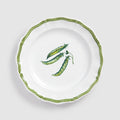 A top-down product photograph of a white round ceramic salad or dessert plate with a delicately scalloped rim, shown against a light gray background. The center features a hand-painted botanical illustration of three green pea pods clustered together, with one pod partially open to show the small peas inside. A thin, wavy green zigzag line traces the exact contour of the scalloped edge.