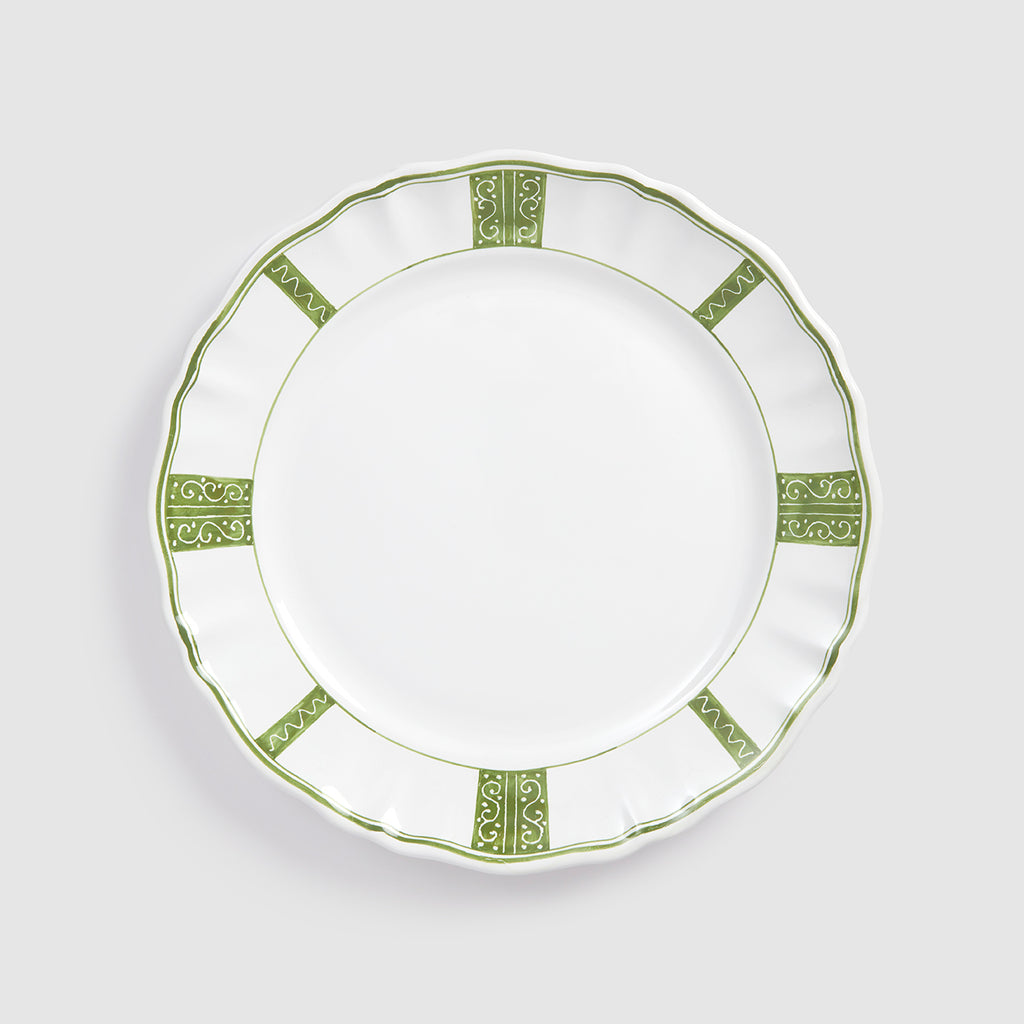 A top-down product photograph of a white round ceramic dinner plate featuring a scalloped rim, shown against a light gray background. The plate's border is decorated with a hand-painted green design consisting of alternating patterns: four rectangular panels filled with intricate swirling scrollwork, and four sections featuring a delicate wavy zigzag border line.