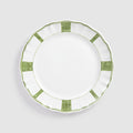 A top-down product photograph of a white round ceramic dinner plate featuring a scalloped rim, shown against a light gray background. The plate's border is decorated with a hand-painted green design consisting of alternating patterns: four rectangular panels filled with intricate swirling scrollwork, and four sections featuring a delicate wavy zigzag border line.