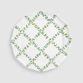 A product photograph of a white round ceramic charger plate, shown flat from a top-down view against a clean, light gray background. The surface of the plate features a hand-painted botanical design with green leafy vines intersecting to form a lattice or diamond grid pattern across the center.